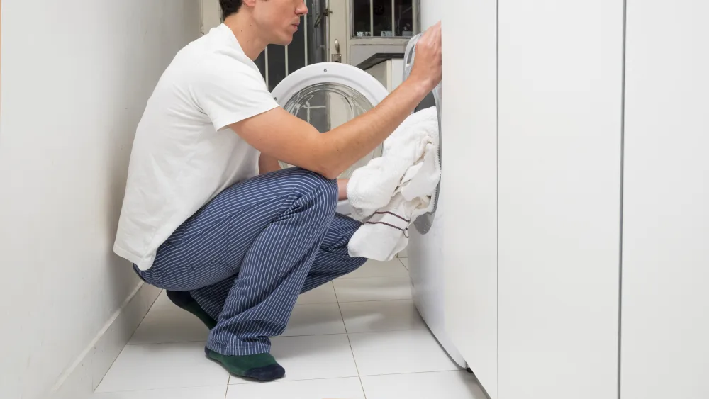 Mann legt Kleidung in die Waschmaschine
